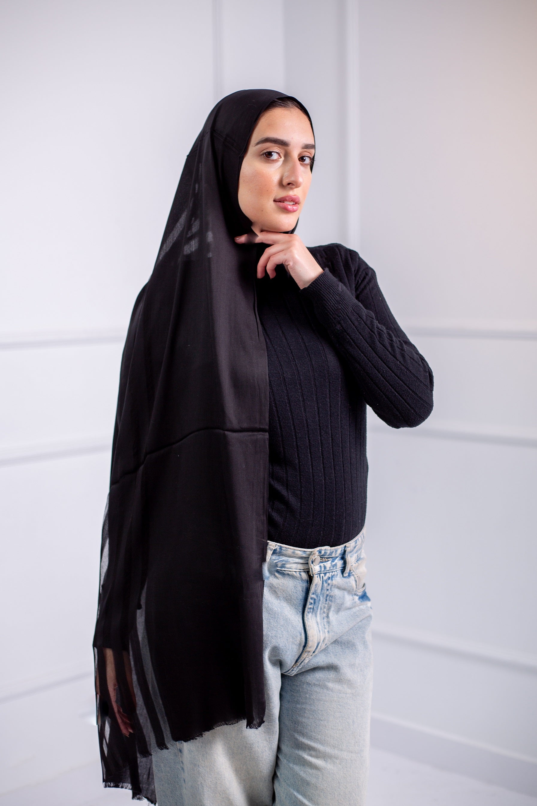 Silky black long hijab with line design, worn with casual jeans and a black top – back view

